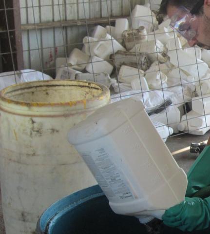 Lucas Burch wears gloves and safety glasses while triple rinsing a pesticide container.